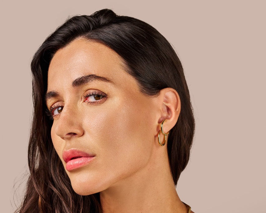 Woman wearing a black top and gold jewelry against a beige background
